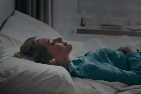 Kvinna med hörlurar i sängen, lyssnar på guidad meditation för avkoppling.