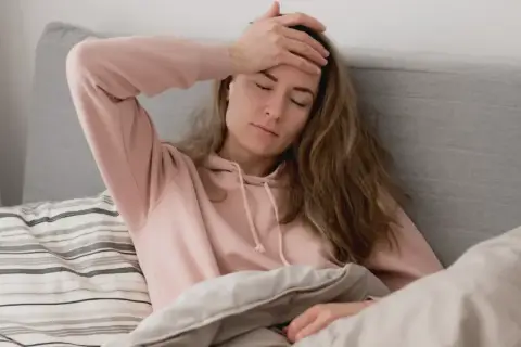 En kvinna med handen på pannan i sängen, känner ångest på morgonen.
