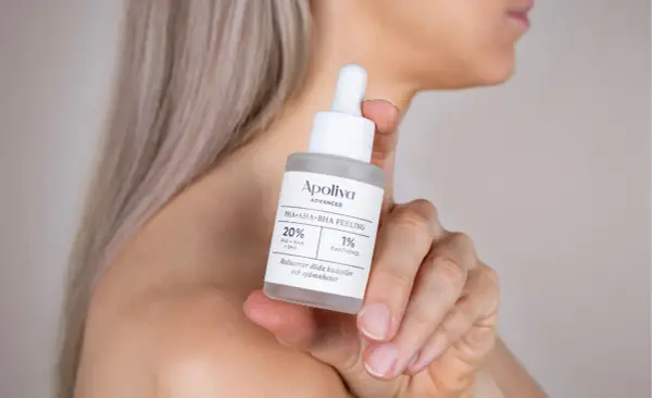 En kvinna håller en flaska med Apoliva PHA+AHA+BHA PEELING. Denna aha syra-produkt hjälper till att reducera döda hudceller.